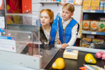 Girl and boy in uniform at the register playing saleswoman, playroom. Kids plays sellers in imaginary supermarket, salesman profession learning