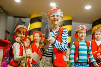 Child in helmet and uniform with hose in hands playing fireman, playroom indoor. Kids lerning firefighter profession. Children lifeguards, little heroes in equipment on playground