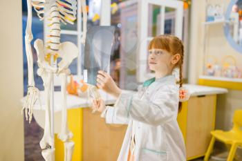 Little girl in uniform looks at the x-ray, playing doctor, playroom. Kid plays medicine worker in imaginary hospital, profession learning, childish dream