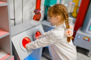 Little girl in uniform playing doctor in laboratory, playroom. Kid plays medicine worker in imaginary hospital lab, profession learning, childish dream