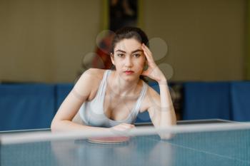 Slim woman poses at the ping pong table indoors. Female person in sportswear, training in table-tennis club