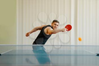 Man with ping pong racket plays the ball off, image in action, workout indoors. Male person in sportswear, training in table tennis club