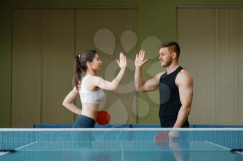 Friends with rackets gives five each other before ping pong tournament indoors. Man and woman in sportswear relaxing in sport club, table-tennis training game in gym