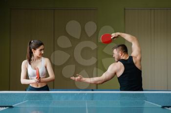 Man and woman on ping pong training indoors. Couple in sportswear holds rackets and plays table tennis in gym. Male and female persons in table-tennis club