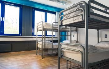 Hostel interior, bunk beds and linen, nobody. Empty sleep motel room, dorm bedroom for travelers and tourists