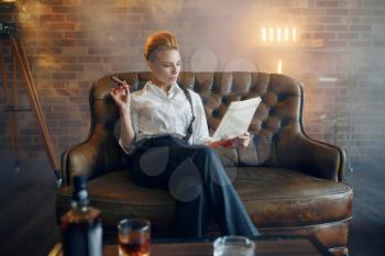 Woman in shirt and trousers reading newspapar with whiskey and cigar, retro fashion, gangster style. Vintage business lady