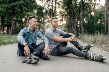 Roller skating, two male skaters sitting on the ground in park. Urban roller-skating, active extreme sport outdoors, rollerskating