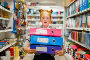 Little school girl holds colorful folders in stationery store. Female child buying office supplies in shop, schoolchild in supermarket