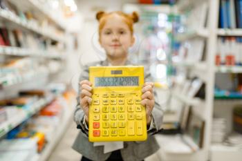 Little school girl with yellow calculator, shopping in stationery store. Female child buying office supplies in shop, schoolchild in supermarket