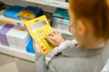 Little schoolgirl holds yellow calculator, shopping in stationery store. Female child buying office supplies in shop, schoolchild in supermarket
