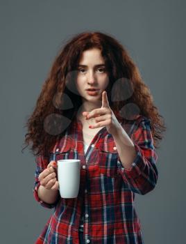 Young pretty woman with cup of coffee on gray background. Adorable redhead girl with wavy hair holds white teacup