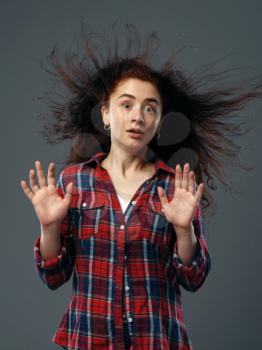 Strong fan blowing in female face, funny emotion. Powerful air flow blows on girl in a shirt, black background