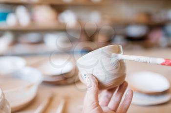 Female potter with brush paints a pot, pottery workshop. Woman molding a bowl. Handmade ceramic art, tableware from clay