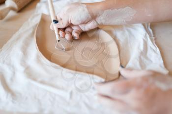 Female potter draws a pattern, pottery workshop. Woman molding working material. Handmade ceramic art, tableware from clay