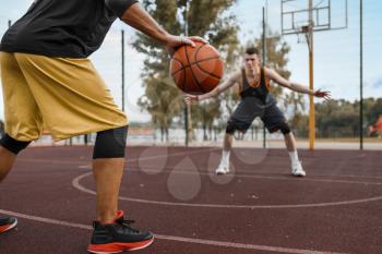 Two basketball players work out tactics on outdoor court. Male athletes in sportswear play the game on streetball training