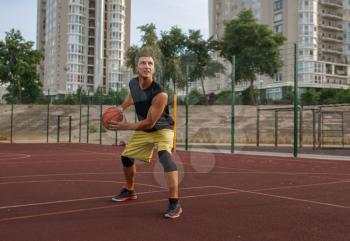 Basketball player prepares to make a shoot on outdoor court. Male athlete in sportswear holds ball on streetball training