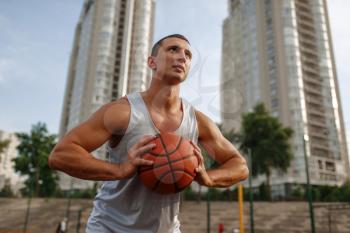 Basketball player aiming for the throw on outdoor court. Male athlete in sportswear holds ball on streetball training