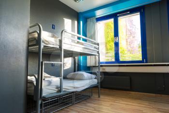 Hostel interior, metal bunk beds and linen, nobody. Empty sleep motel room, dorm bedroom for travelers and tourists