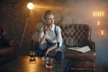 Woman in shirt and trousers sitting at the table with whiskey, retro fashion, gangster style. Vintage business lady