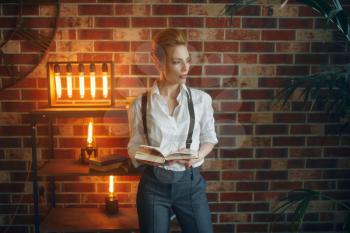 Business woman in strict clothes poses with book in studio, retro fashion, gangster style. Vintage lady in office with brick walls