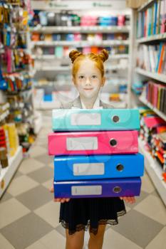 Little school girl holds colorful folders in stationery store. Female child buying office supplies in shop, schoolchild in supermarket