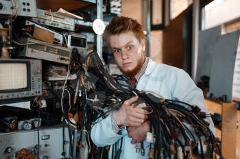 Strange engineer holds bunch of wires with different plugs in laboratory. Electrical testing tools on background. Lab equipment, engineering workshop