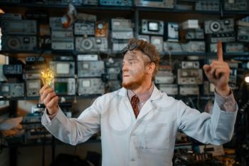 Strange scientist with a burning light in his hands, test in laboratory. Electrical testing tools on background. Lab equipment, engineering workshop