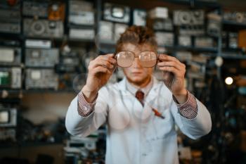 Strange scientist looks through the glasses in laboratory. Electrical testing tools on background. Lab equipment, engineering workshop