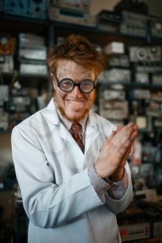 Crazy male scientist in glasses conducts a test in laboratory. Electrical testing tools on background. Lab equipment, engineering workshop