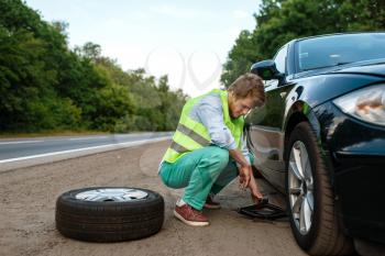 Car breakdown, young man repairing flat tyre. Broken automobile or problem with vehicle, trouble with punctured auto tire on highway