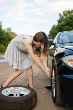 Car breakdown, young woman puts the spare tyre. Broken automobile or problem with vehicle, trouble with punctured auto tire on highway