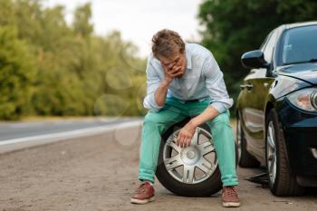 Car breakdown, tired man sitting on spare tyre. Broken automobile or problem with vehicle, trouble with punctured auto tire on highway