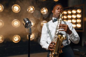 Male jazz performer plays the saxophone on the stage with spotlights. Black jazzman preforming on the scene