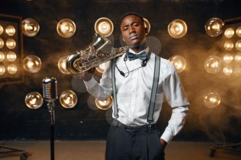 Black male jazz performer poses with saxophone on the stage with spotlights. Black jazzman preforming on the scene