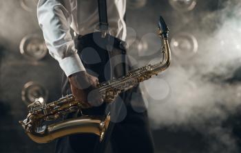 Black jazz musician with saxophone on the stage with smoke. Black jazzman holds instrument in hands