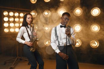 Male jazzman and female saxophonist with saxophone on the stage with spotlights. Jazz performers playing on the scene
