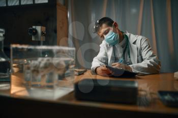 Male psychiatrist in mask and glasses sitting at the table, mental hospital. Doctor in clinic for the mentally ill
