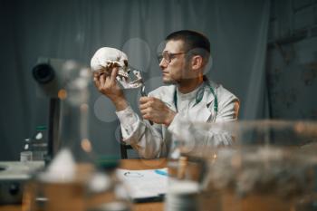 Male psychiatrist in lab coat examines the human skull, mental hospital. Doctor in clinic for the mentally ill
