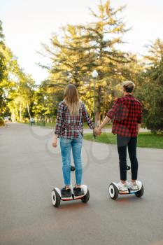 Young couple riding on gyro board in park, back view. Outdoor recreation with electric gyroboard. Transport with balance technology