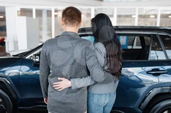 Couple choosing new car in showroom, back view. Male and female customers looks vehicle in dealership, automobile sale, auto purchase