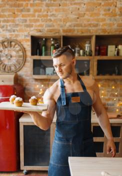 Nude husband in apron holds tray with sweet dessert on the kitchen. Naked male person preparing breakfast at home, food preparation without clothes