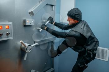 Bank robbery, male robber in black uniform trying to break vault lock. Criminal profession, theft concept