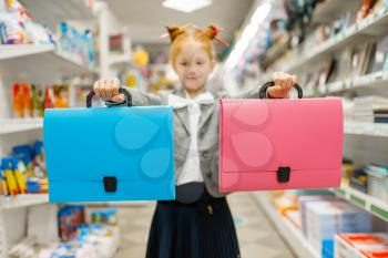 Little school girl with two folders in stationery store. Female child buying office supplies in shop, schoolchild in supermarket
