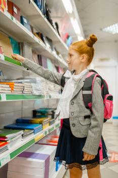 Little school girl with backpack at the shelf in stationery store. Female child buying office supplies in shop, schoolchild in supermarket