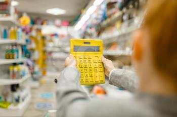 Little schoolgirl holds yellow calculator, shopping in stationery store. Female child buying office supplies in shop, schoolchild in supermarket