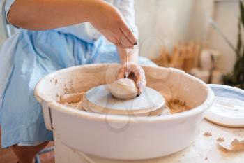 Female potter hands works on pottery wheel. Woman molding a pot. Handmade ceramic art, tableware from clay