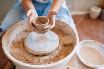 Female master holds wet pot over the pottery wheel. Woman molding a bowl. Handmade ceramic art, tableware from clay