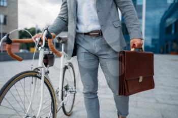 Businessman in suit with briefcase and bicycle in downtown closeup. Business person riding on eco transport on city street