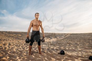 Male athlete doing exercises with two kettlebell in desert at sunny day. Strong motivation in sport, strength outdoor training