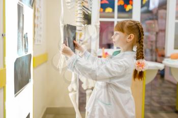 Little girl in uniform looks at the x-ray, playing doctor, playroom. Kid plays medicine worker in imaginary hospital, profession learning, childish dream
